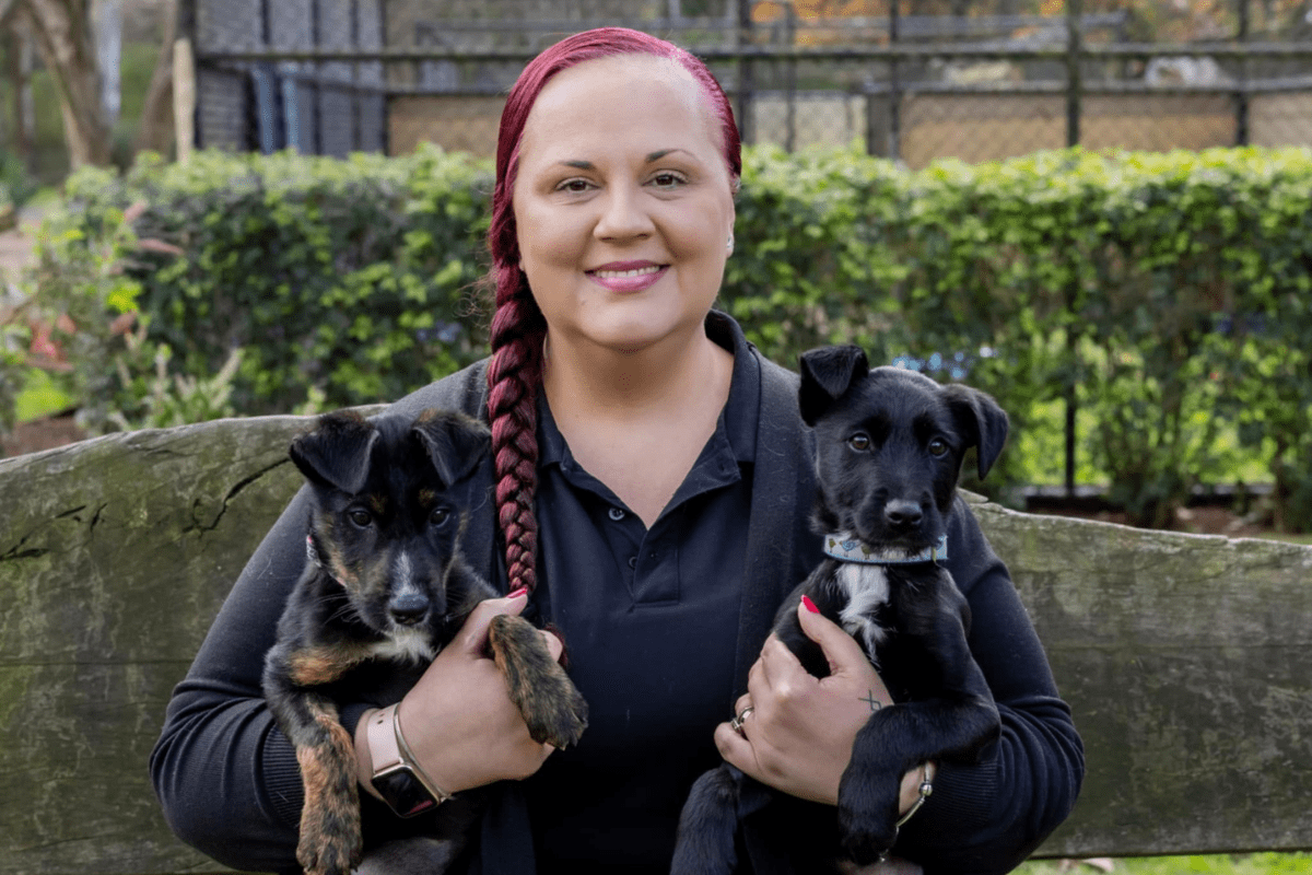 A smiling woman holding a dog in each arm